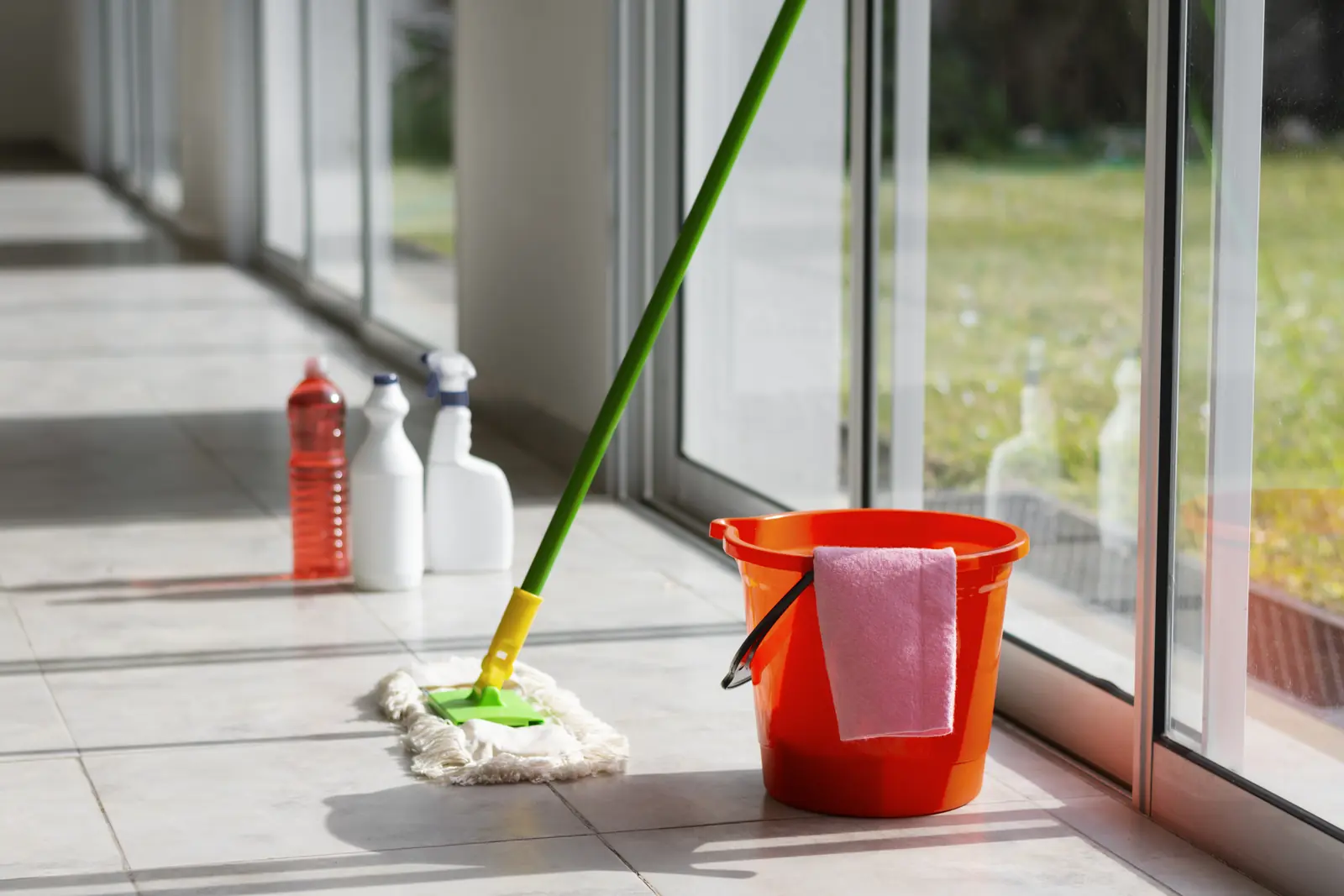 Mop and bucket on a bright tiled floor beside large windows